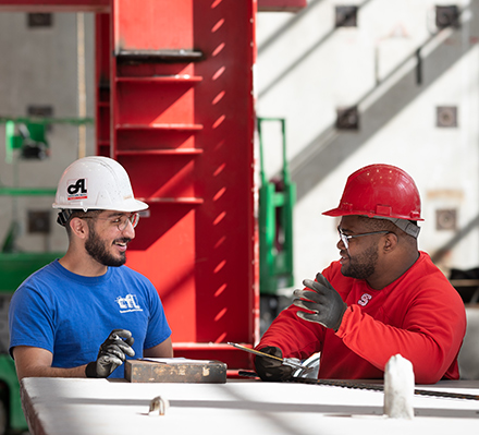 two men in red hard hats working at a table in a warehouse